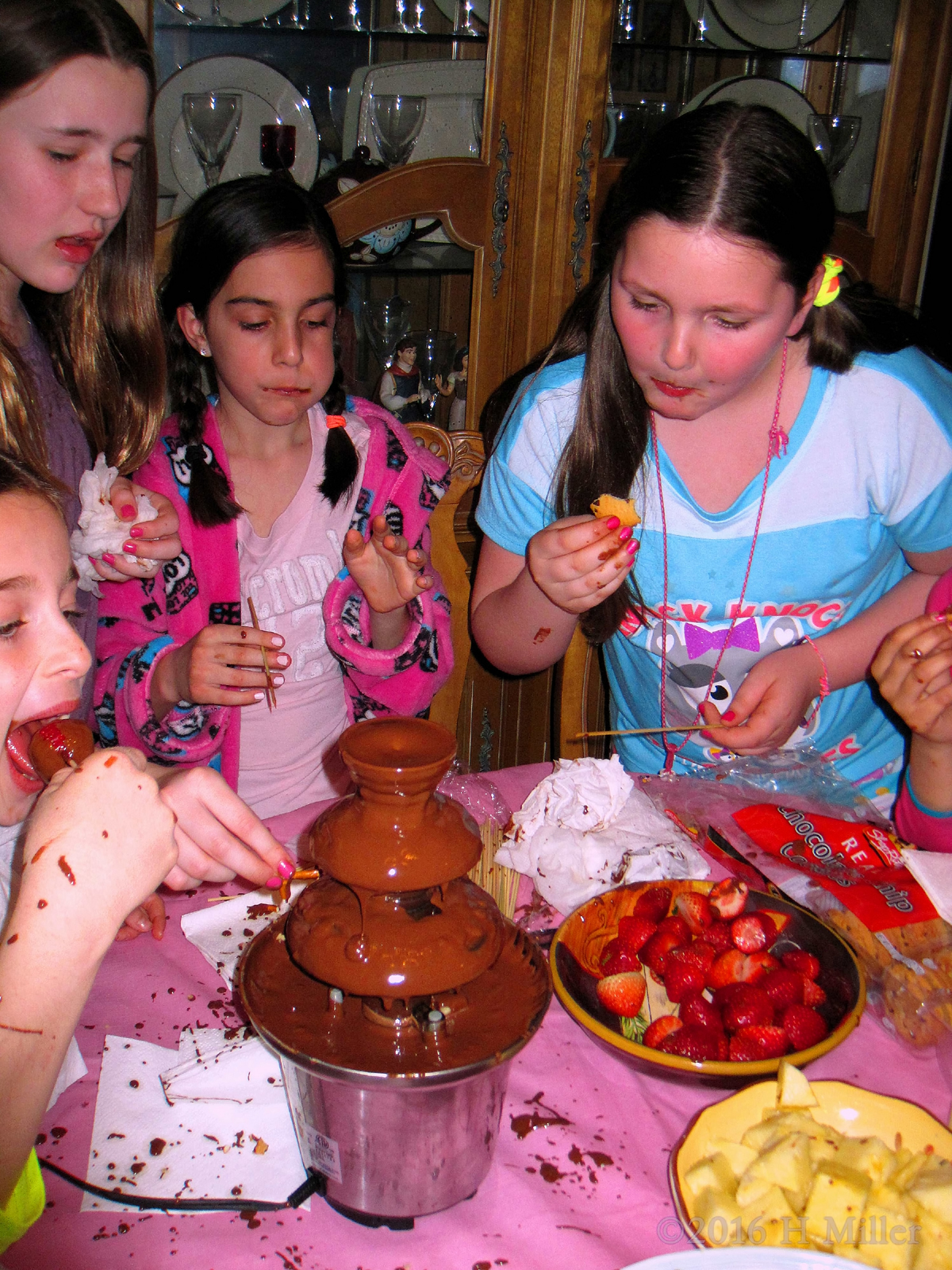 A Picture Capturing The Party Guests Enjoying The Chocolate Fondue Fountain And Snacks 
