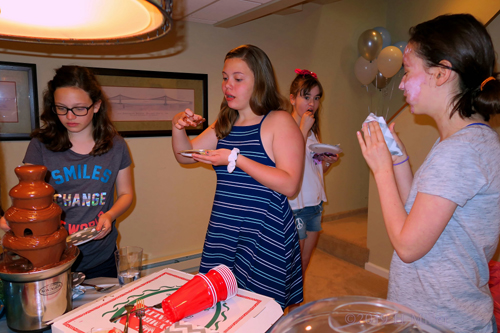 Girls Standing Around The Chocolate Fountain Eating Snack Girls Standing Around The Chocolate Fountain Eating Snack